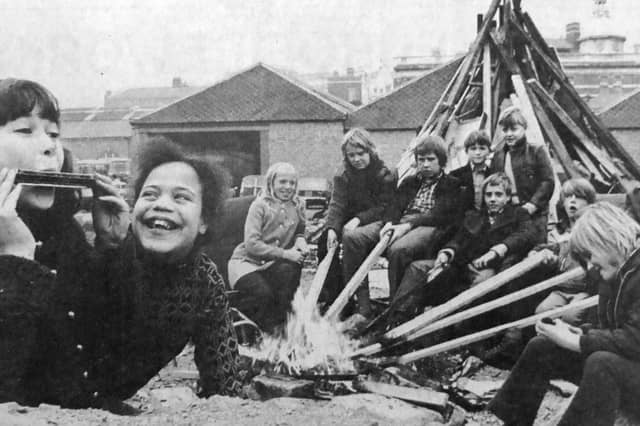 Children sit near their bonfire at Hyde Park Road, Southsea, roasting potatoes on a small fire, with Sally Farley, 10, on the mouth organ
