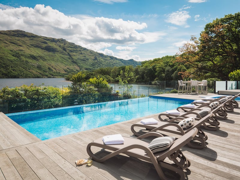 Sun loungers are arranged alongside the home's outdoor pool, with views towards Loch Lomond.