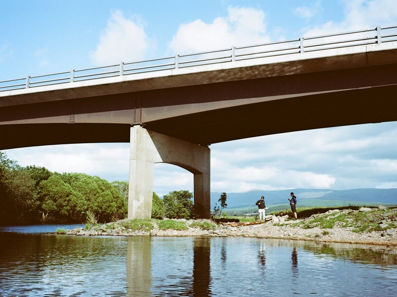 A couple of local teenagers fish on the River Spey beneath a road bridge of the A9
