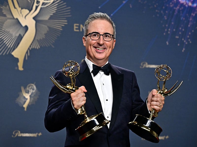 British television host John Oliver poses in the press room with the awards for Outstanding Writing for a Variety Series and Outstanding Scripted Variety Series award for "Last Week Tonight With John Oliver" during the 77th Primetime Emmy Awards.
