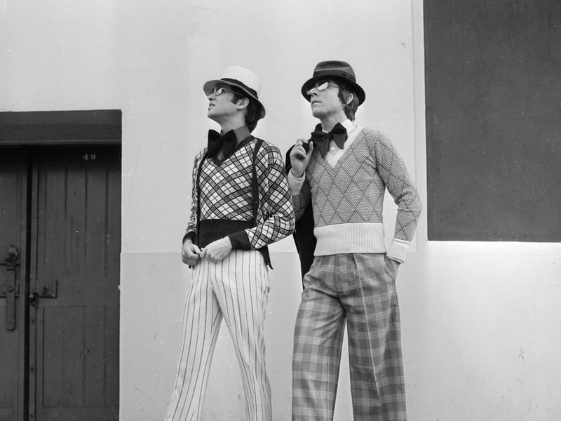 One model is seen here in 1973 sporting a brown and cream plaid twin set by John Craig, while beside him another wears a diamond-patterned sweater by Azzura, and Oxford bags by Monte Cristo