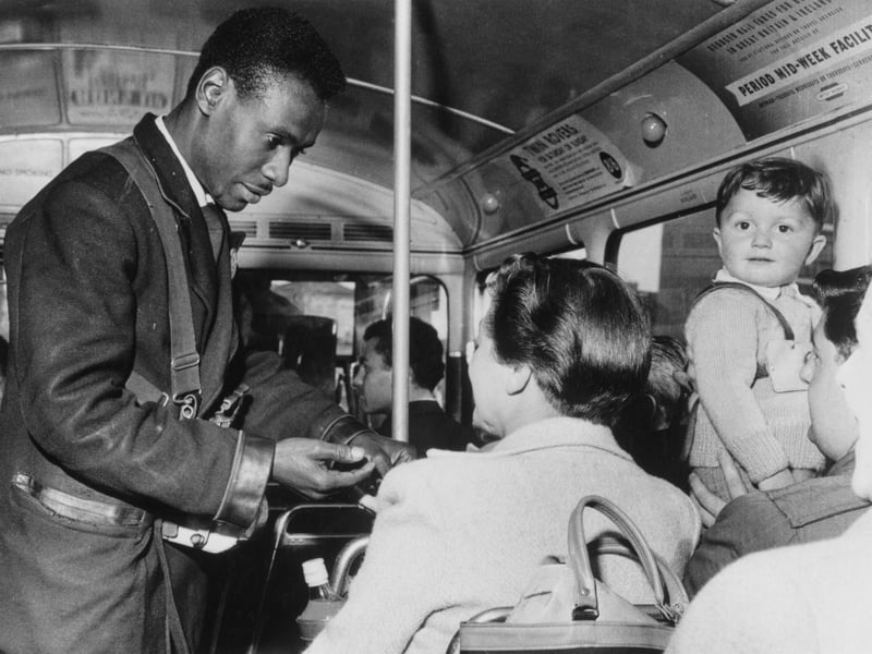 A bus conductor holds out his hand as he collects the fare from a passenger in around 1965