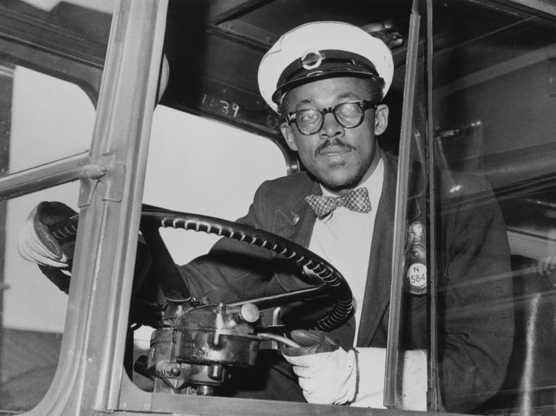 A bus driver at the wheel, wearing a checked bow tie, in around 1965