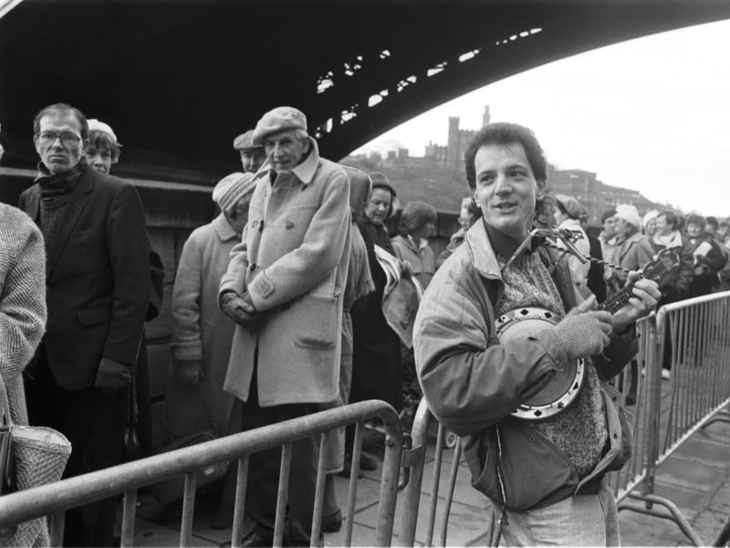A busker plays the banjo for a long queue of people waiting to see the Gold of the Pharaohs exhibition at the City Art Centre in February 1988