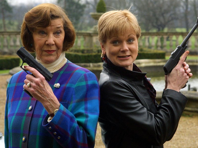 The first Miss Moneypenny, Lois Maxwell, and the current, Samantha Bond, pose with guns used in earlier James Bond movies, in February 2000