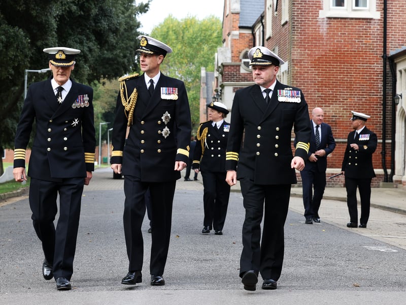 HRH Duke of Edinburgh walking with Royal Navy officers.