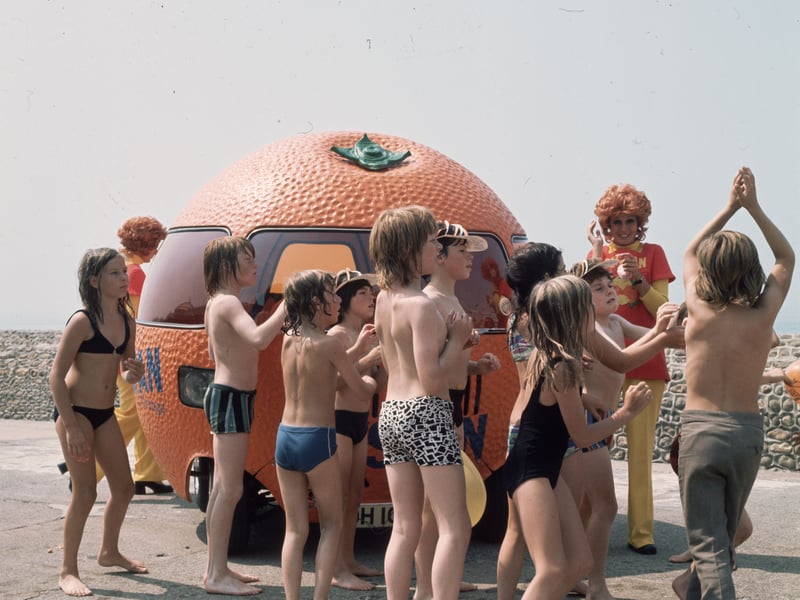 Children gather around a large motorised clockwork orange advertising 'Outspan' South African oranges in August 1973