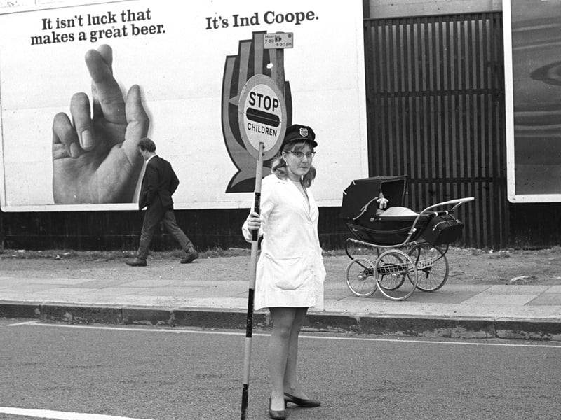 A lollipop lady standing in front of a billboard advertising Ind Coope beer, in 1970