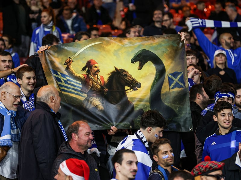 A Greece fan holds up a banner that depicts the Loch Ness Monster in battle.