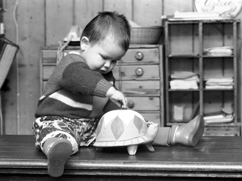 Baby Nico modelling children's fashions from Azteca, playing with a tortoise money bank on the counter of the Edinburgh shop, on St Stephen Street, in December 1988