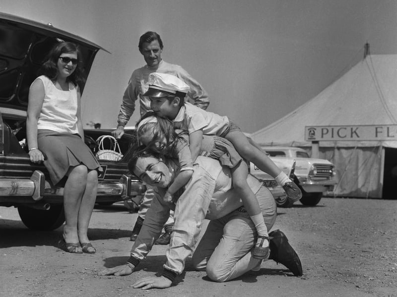 British motor-racing champion Jackie Stewart plays with Graham Hill's children, Brigitte and future champion Damon, at Silverstone, while their father watches their antics from nearby, in May 1965
