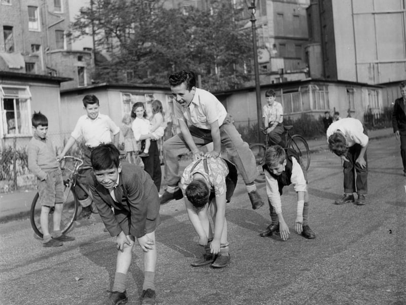 Youngsters playing leap-frog in the street, watched by their friends, in October 1955
