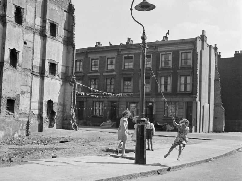 Children swinging on a lamppost beside a demolished terraced house in the early 60s