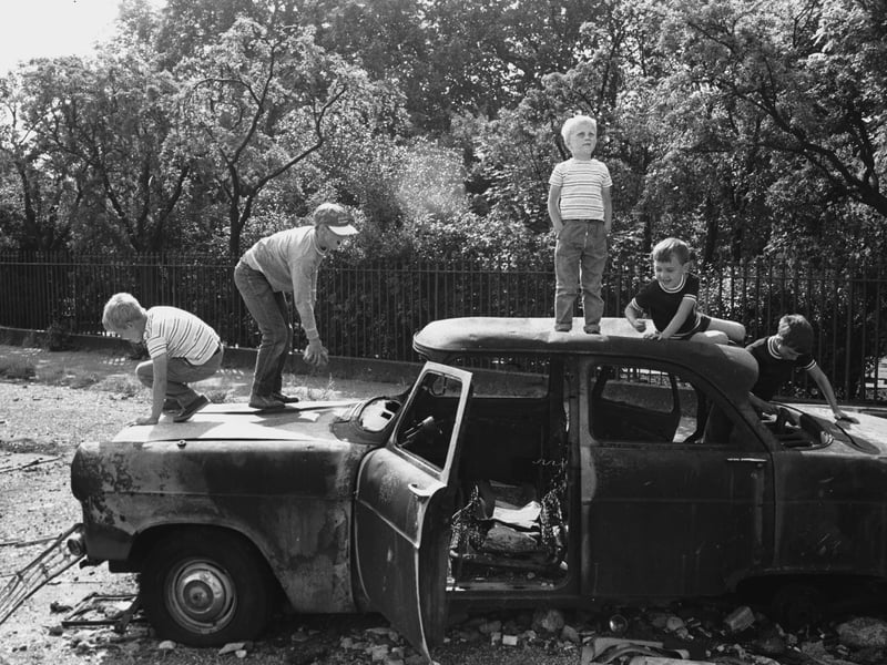 Boys clamber over an abandoned car in the 1960s