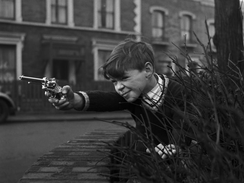 A boy hiding amid the shrubbery takes aim with a toy pistol in February 1958