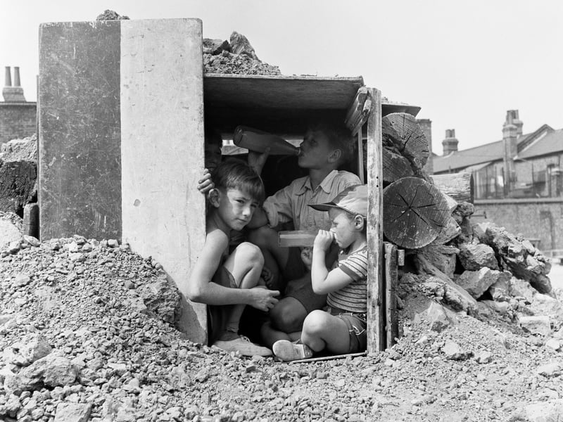 Children play inside a den amid the rubble in August 1955