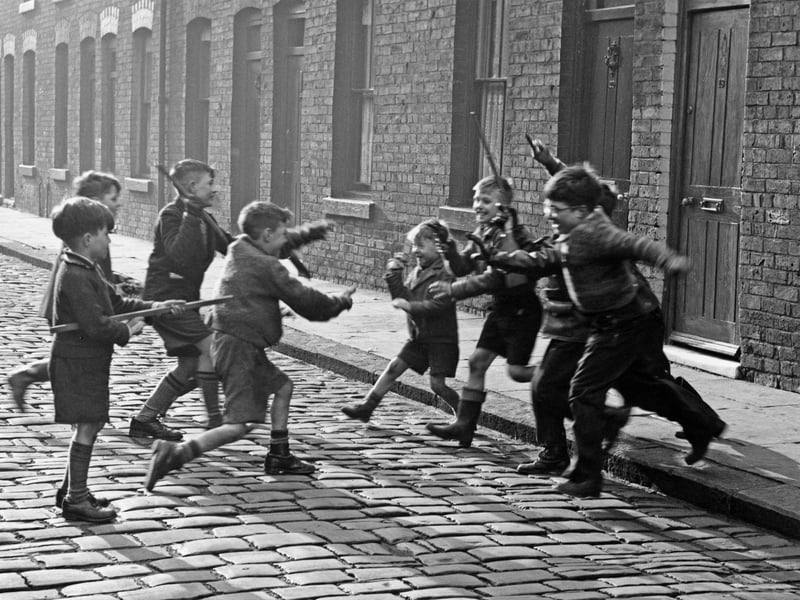 Children playing a game of 'cowboys and Indians' on a cobbled street in Salford in 1957