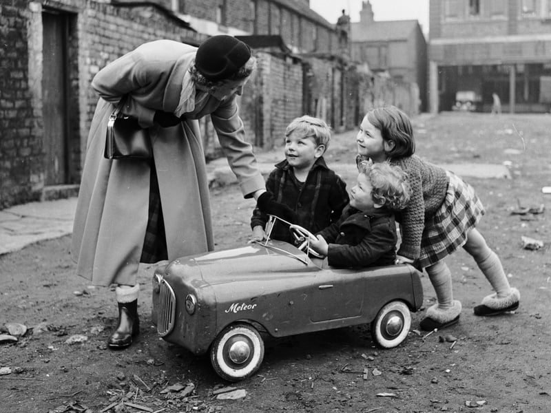 Peggy Robertshaw stops to talk to three children as she walks her daily 12 miles around Liverpool, testing shoes for Dunlop of Speke, in January 1965
