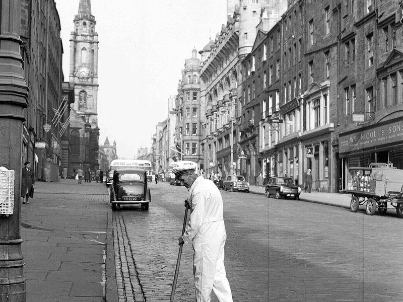 A street orderly in a white uniform using an old besom broom to clean the High Street  Royal Mile, in Edinburgh, in 1956.
