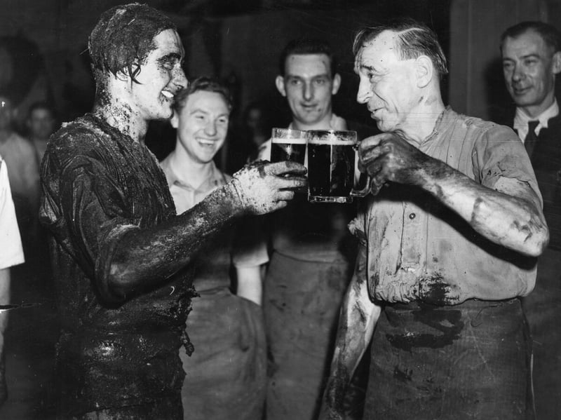 1st September 1950:  P Newton, right, toasts his pupil, apprentice cooper R A Barban, after his passing out ceremony at Watney's Stag Brewery, in Mortlake, London, in September 1950. During the ceremony, called 'trussing the cooper',  the cooper is encased in his own barrel, has various concoctions including beer poured over him and is rolled around the brewery in the barrel.
