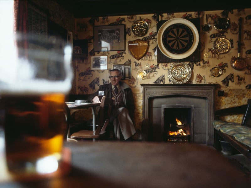 A man enjoys a quiet pint of ale by a real fire in a country pub in Beckhole, Yorkshire, in around 1982