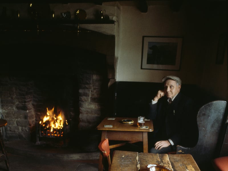 A man enjoys a quiet pint of ale by a real fire in the cosy atmosphere of the Forresters Arms country pub in the rural village of Carlton, North Yorkshire, in April 1982