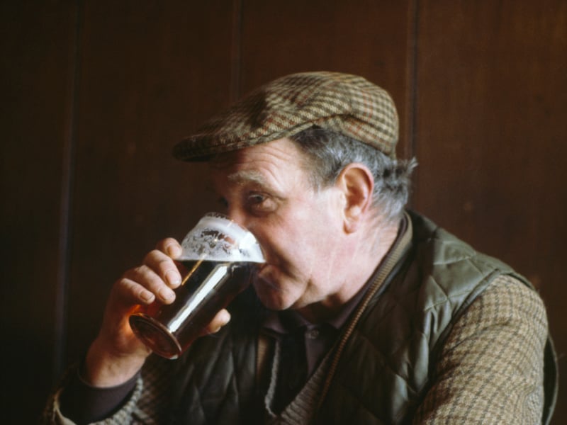 A man in a flat cap enjoys a pint of ale in the Victoria Arms, a rural pub in Worton, Yorkshire, in around 1982