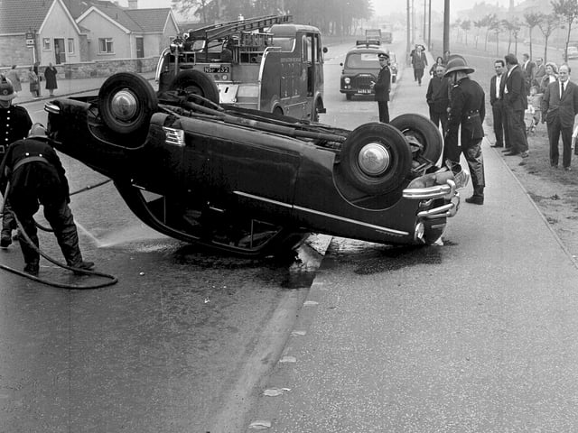 Firemen wash spilt petrol off the road after a car crash in Edinburgh in 1964. 