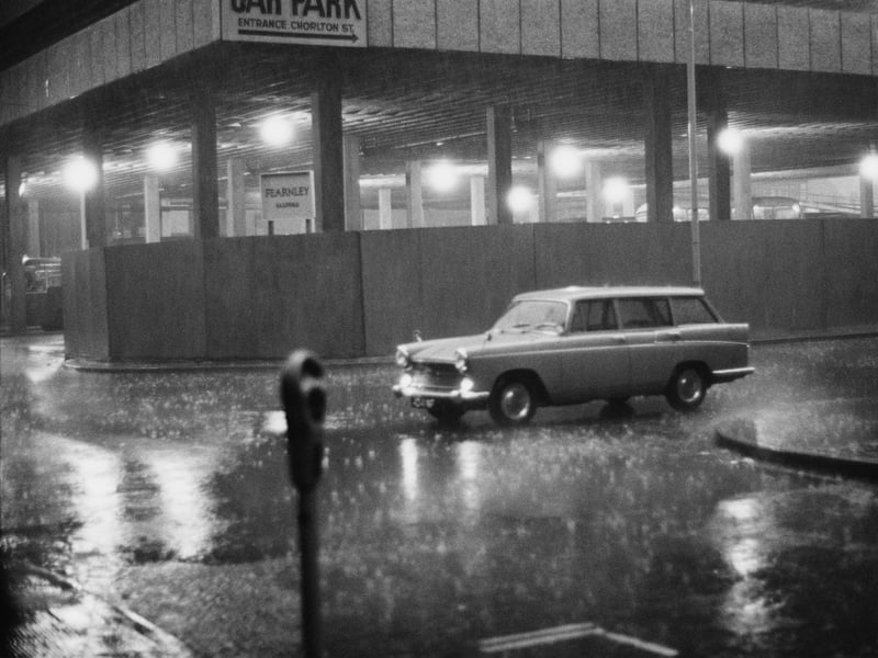 A Morris Oxford outside a multi-storey car park on a rainy night in Manchester, in around 1960