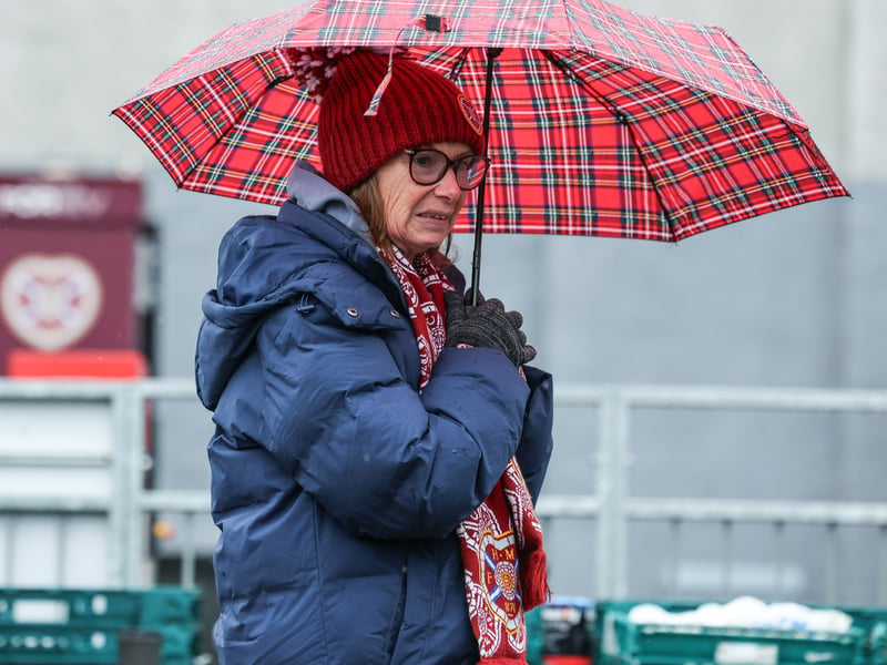 A Hearts fan keeps herself dry as the rain teems down ahead of kickoff.