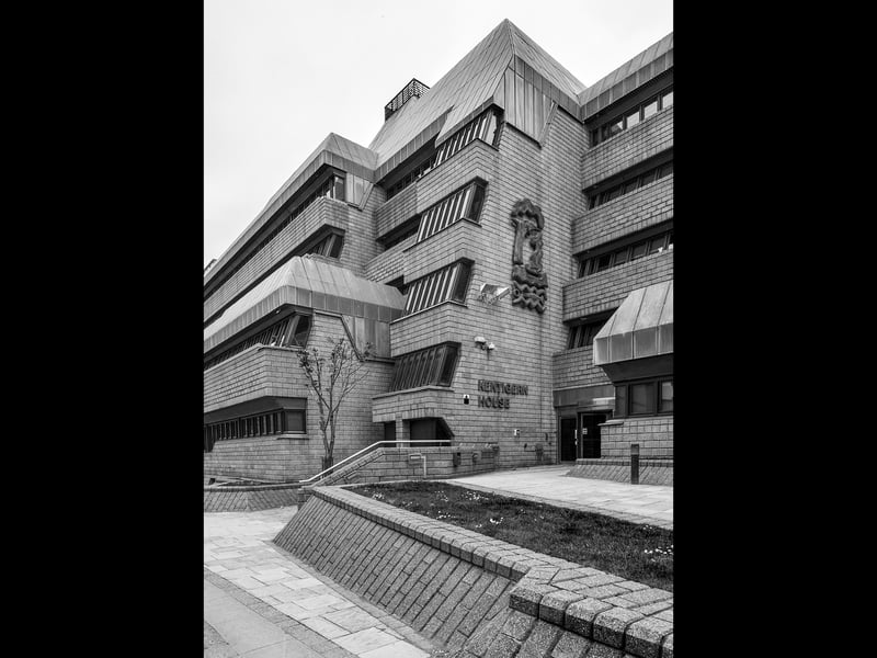 Kentigern House, designed by the Property Services Agency for the Ministry of Defence and built between 1981 and 1986, is a large government office complex. Its ziggurat design is functional and austere, characterised by staggered concrete block elevations, repetitive strip glazing, and a strong sense of order. The building’s scale and materials reflect the institution
housed within fostering a fortified bunker appearance in recognition of the terrorist threats existing at the time of construction. There is an almost sculptural discipline in the way levels, stair-towers, entrances and angled-glazing intersect, producing shadows that accentuate structural geometry. Kentigern House carries the quiet weight of authority; refusing ornament, its concrete and enduring repetition speaking the language of state power.