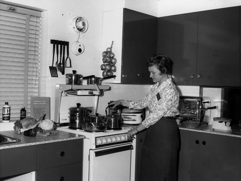 A woman puts the kettle on in a model kitchen in the Ideal Home Exhibition in March 1961