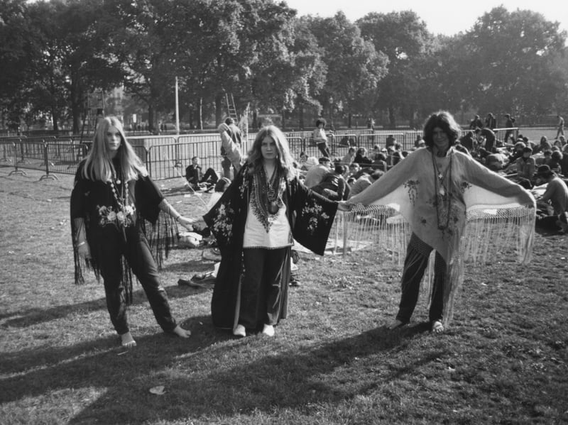 Three hippies, wearing fringed shawls, hold hands at a pop concert in Hyde Park, London