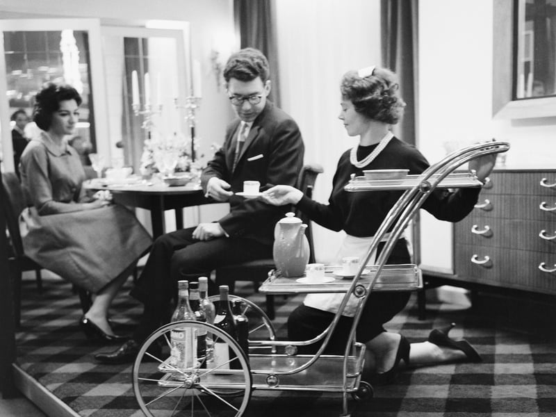 A woman serves tea from a trolley to diners on a stage at a furniture exhibition in February 1960