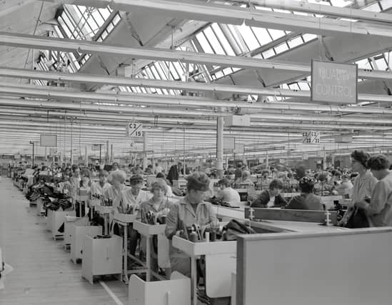 A photo of No2 Coat Room The image shows the factory floor with women sewing at the machines. The sign hanging from the ceiling above reads 'quality control'.
