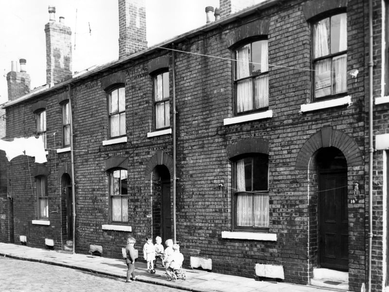 Three houses on Oldfield Street. Number 18 is on the left, 16 in the centre and 14 to the right. A group of children are playing with various toys. Pictured in November 1964.