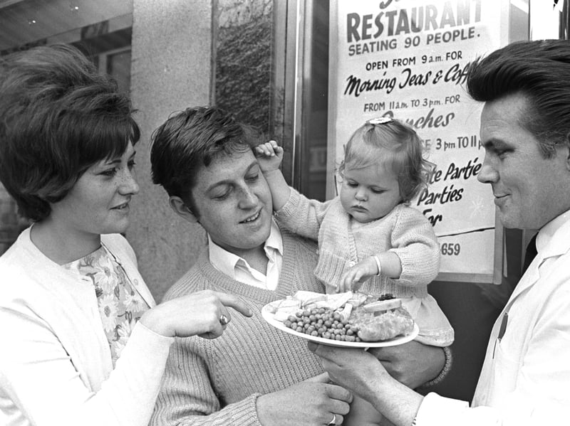 A waiter brings a plate of fish, chips and peas to a family outside a restaurant in around 1970
