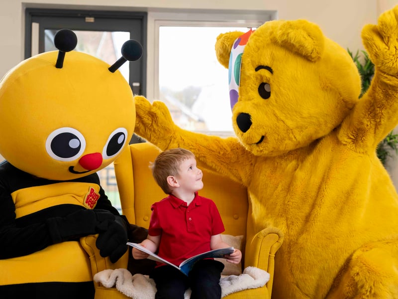 A youngster enjoys reading with Pudsey Bear and Busy Bee.