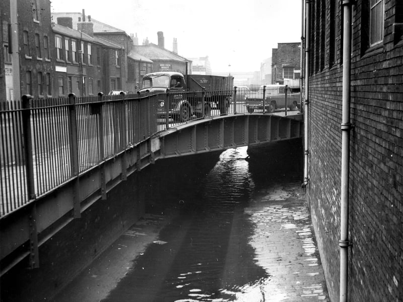 This view shows the Globe Road bridge over Hol Beck, seen in the centre of the photo. Water Lane is to the left. Among buildings in the background is the Hide and Skin Market at no.105 Water Lane. Pictured in November 1965.