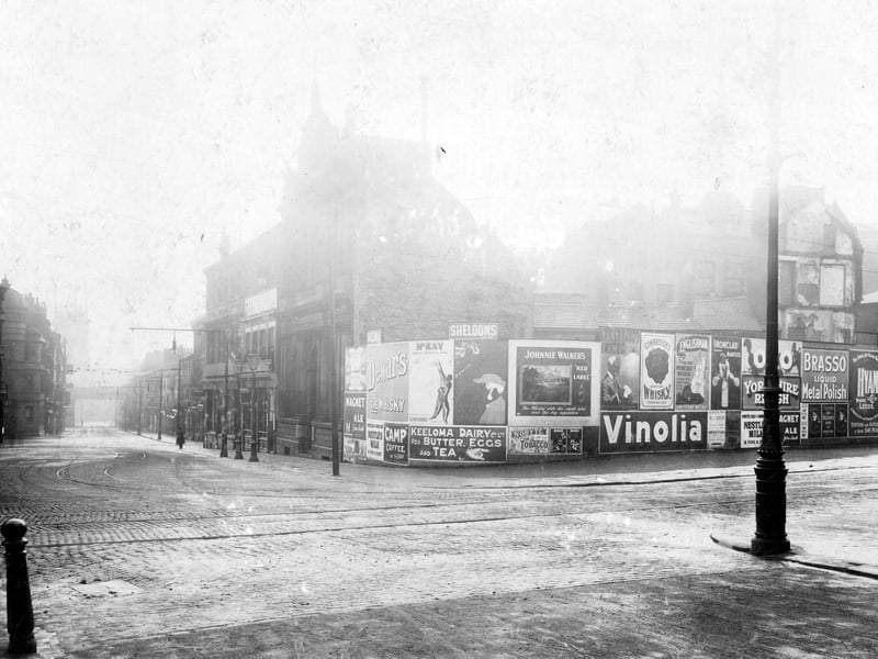 The junction of Vicar Lane and Kirkgate. Sheldon's advertising hoardings on corner with various adverts. Photo is looking down Kirkgate with Market buildings on the left. The railway bridge with St. Peter's Church can just be seen in distance.