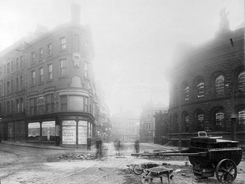 Looking north-east along Call Lane from the junction with Duncan Street, showing New Market Street leading off to the left. The building on the corner appears to be empty with notices saying that previous occupants James Cavanagh & Co., wholesale glass and china merchants, have removed to Lady Bridge Mills, Lady Lane. On the right is part of the Corn Exchange.
