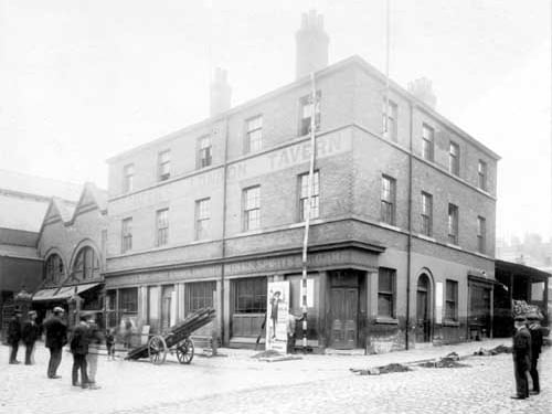 A view of the derelict building that was Coldbecks London Tavern at 32 George Street. The entrance to the wholesale fish market is on the left. Men stand on the cobbled street. Pictured in August 1908.