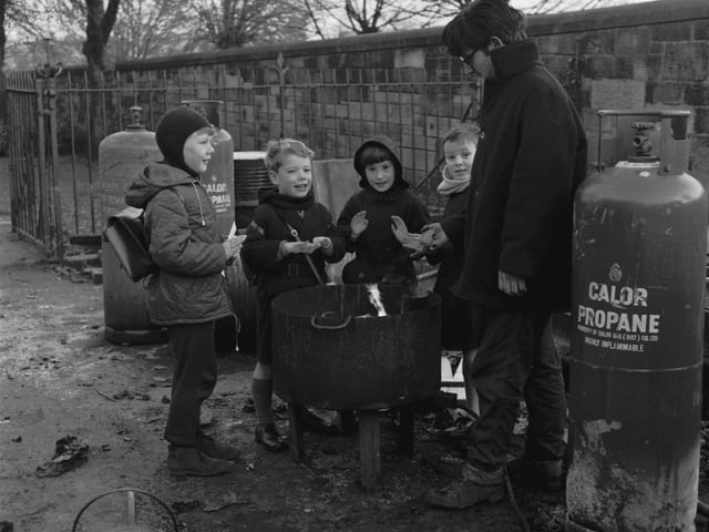 Four children warm themselves at a workman's propane brazier (a workman's fire) in Morningside Drive in November 1965.