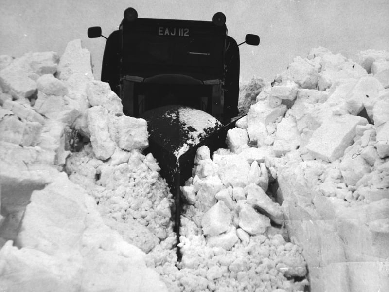 A 10-ton snow plough carves its way through drifts on the Reeth Brough Road that have been cut up into large blocks by workmen, scattering them like toy bricks, in January 1963