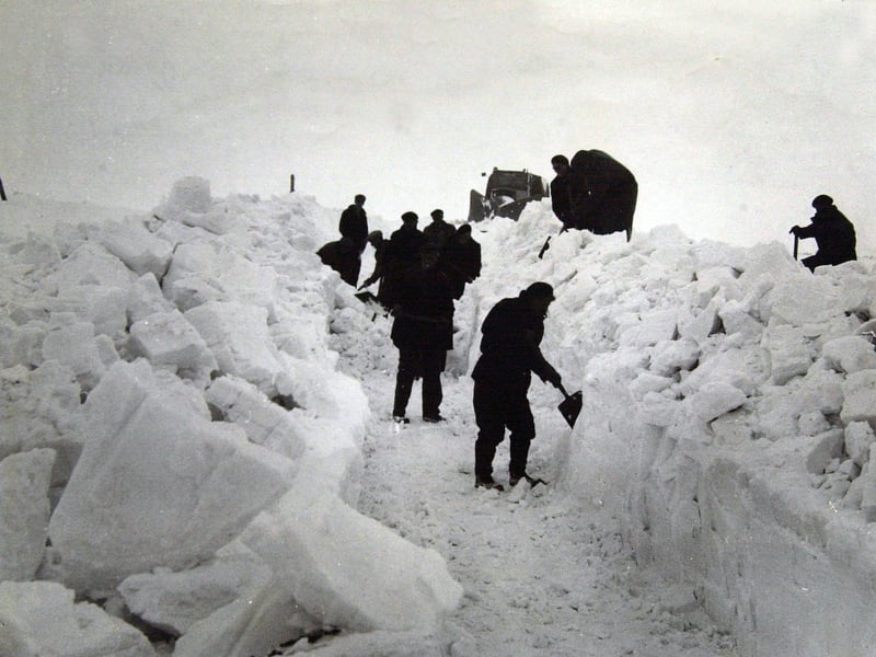 A snow plough and workers with shovels clear a path at Tan Hill, Yorkshire, in January 1963