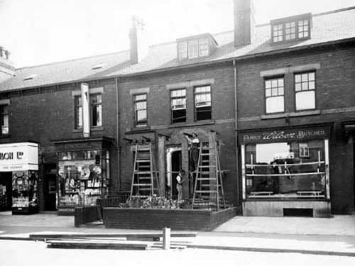 A row of shops on Austhorpe Road. From left to right is a general store (unidentified), J. Hinchcliffe, chemist amd pharmacist, No 40 in process of being altered / renovated, and Wilson family butcher. 2 workmen with ladders working on no 40. Pictured in July 1935.
