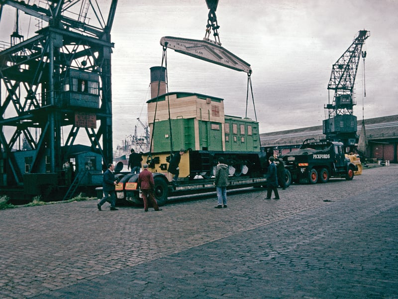 This image shows a diesel locomotive built in Kilmarnock by Andrew Barclay Sons & Co. being delivered to the King George V Dock for shipment to East Africa in 1971. Here the locomotive, built for the East African Railways and Harbours, is being lifted by the floating crane ‘Newshot’