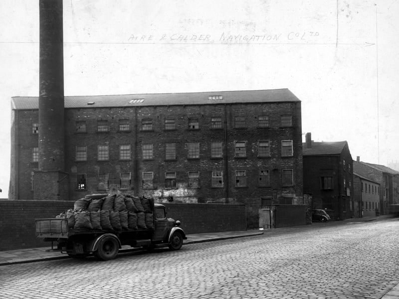 The mills and factories on the south west side of East Street. A road is in front of the mill with a large coal truck parked on it, with 'J.H.Hudson', painted on the door. To the right of the picture is a car parked in a driveway. The factory's chimney can be seen clearly on the left. Pictured in November 1948.