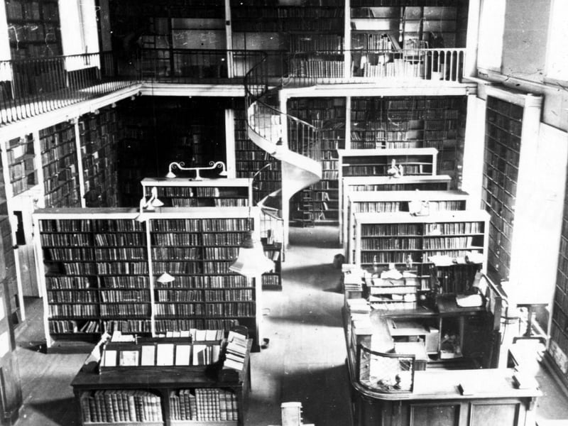 The inside of Leeds Library on Commercial Street in October 1948. Shelves of books, the counter and a spiral staircase are visible.