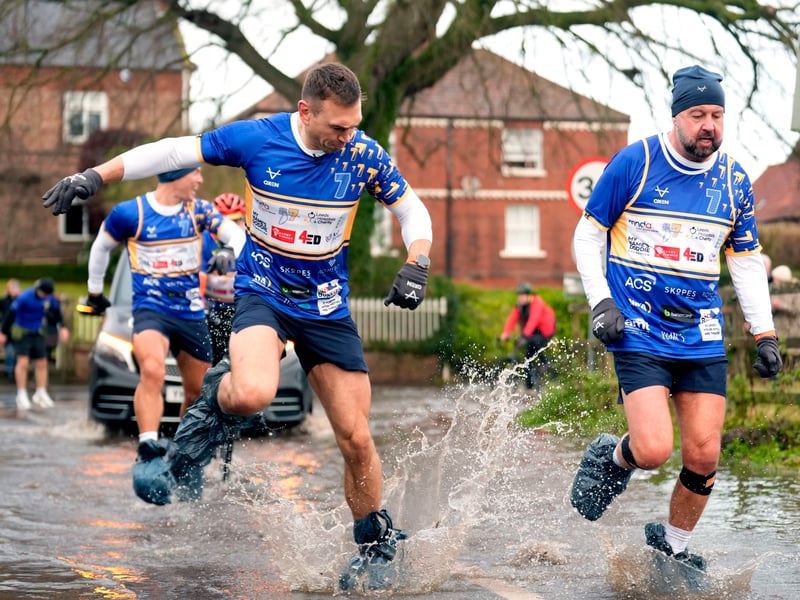 Kevin Sinfield sporting bin bags to cover his footwear as he runs through flood water in Cattal.